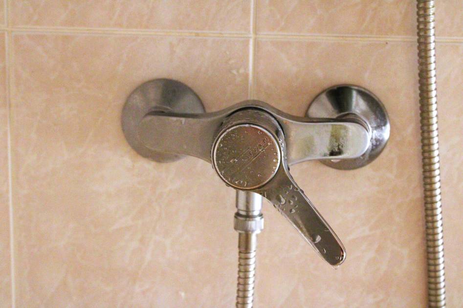 Close-up of a handheld shower head with chrome finish against a tiled bathroom wall